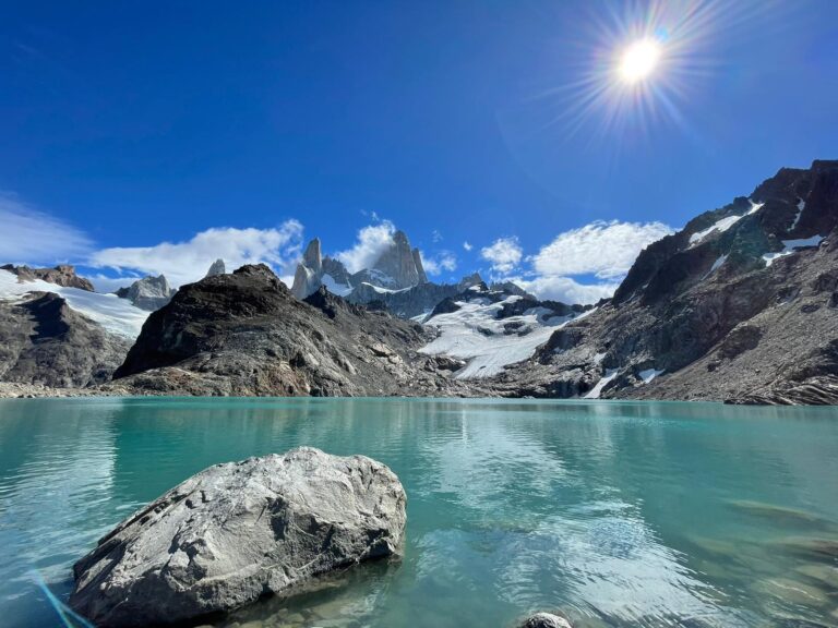 View of Laguna de los Tres with turquoise glacier-fed water beneath the jagged peaks of Mount Fitz Roy in Patagonia, Argentina, surrounded by rocky terrain and a clear blue sky.